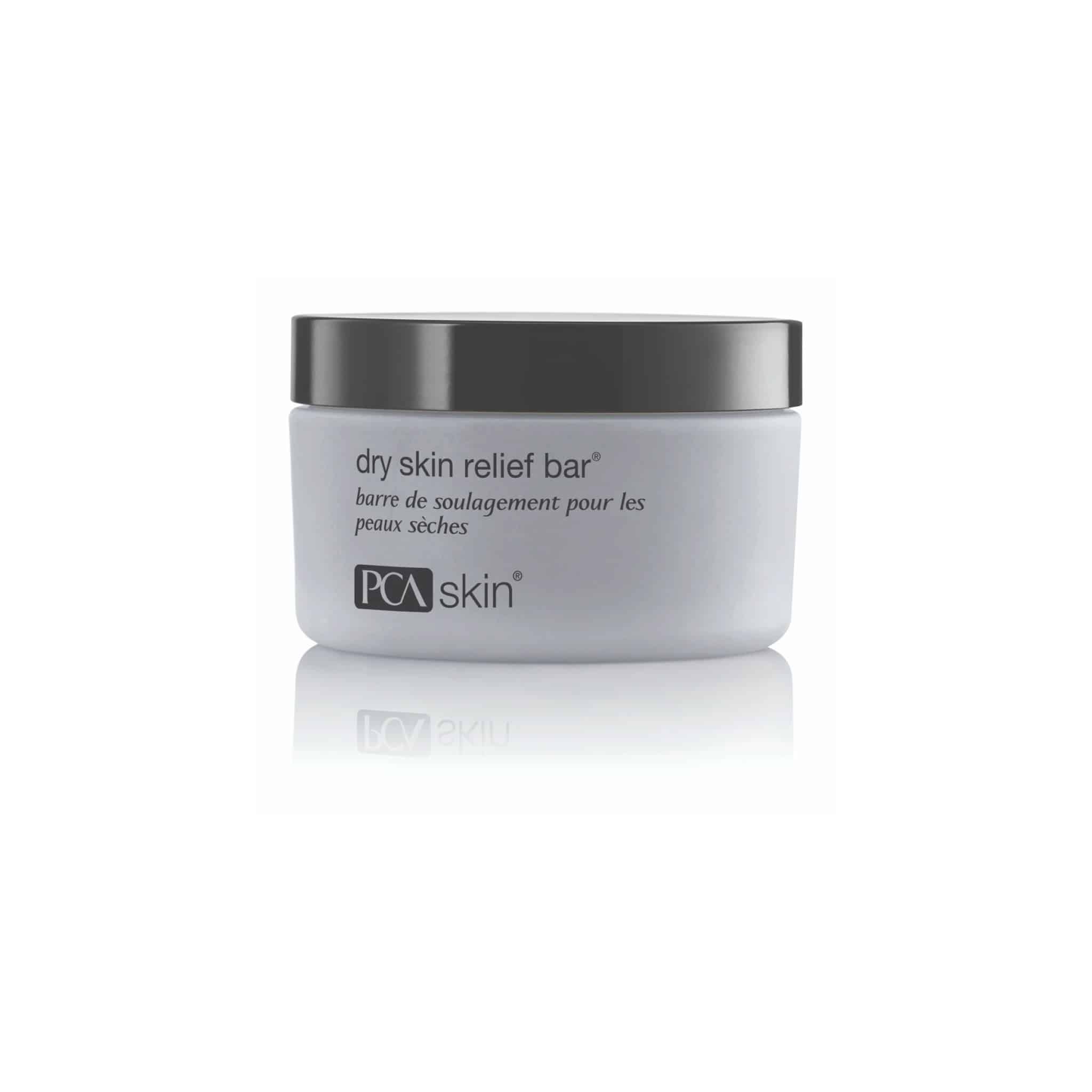 A white container with a black lid, labeled "Dry Skin Relief Bar" and "PCA Skin." The label includes both English and French text, with the French translation below the English description. This gentle cleansing bar is designed for skincare, ideal for those with dry skin.