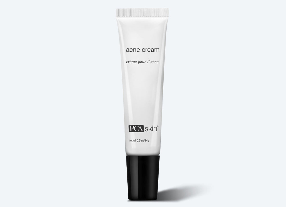 A white tube of Acne Cream with a black cap is displayed against a light grey background. The words "acne cream" and "crème pour l&