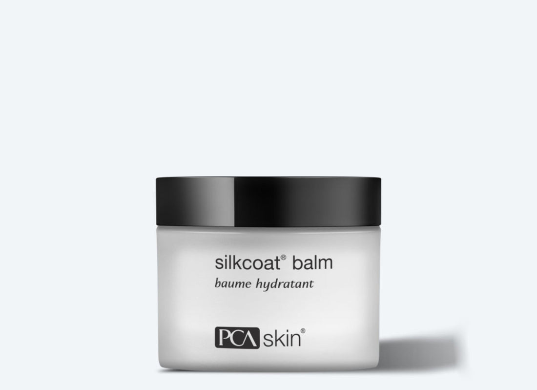 The image shows a jar of Silkcoat Balm, an advanced moisturizer designed for ageing skin. The white jar with a black lid features text that reads "silkcoat® balm," "baume hydratant," and bears the PCA Skin logo. The light gray background accentuates the jar&