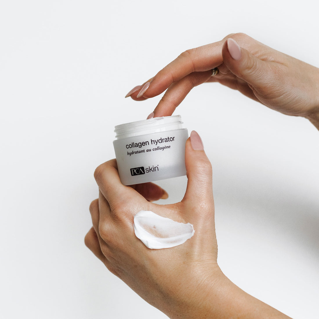 A person dips fingers into a jar of Collagen Hydrator 48g, holding it with a cotton pad and some cream against a white background—ideal for delivering intense hydration to mature skin.