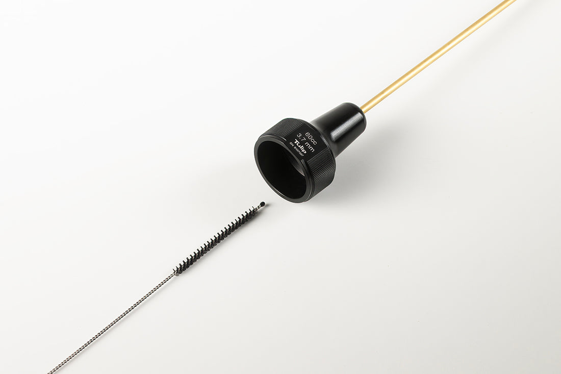 A close-up image of a brass tube with a black cap and a small cleaning brush featuring nylon bristles placed next to it on a white background. The tube appears to be part of the CellFriendly Instrument Cleaning Brushes™ kit, and the brush is likely used for cleaning the inside of the tube.