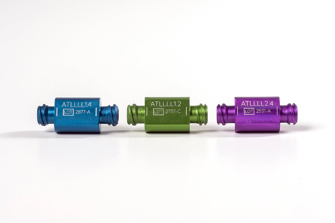 Three small, cylindrical, metallic connectors in blue, green, and purple are lined up horizontally on a white background. Each Anaerobic & Sizing Transfers™ connector is labeled with a code: "ATL1114," "ATL1112," and "ATL1124" respectively, along with additional lot numbers and details.