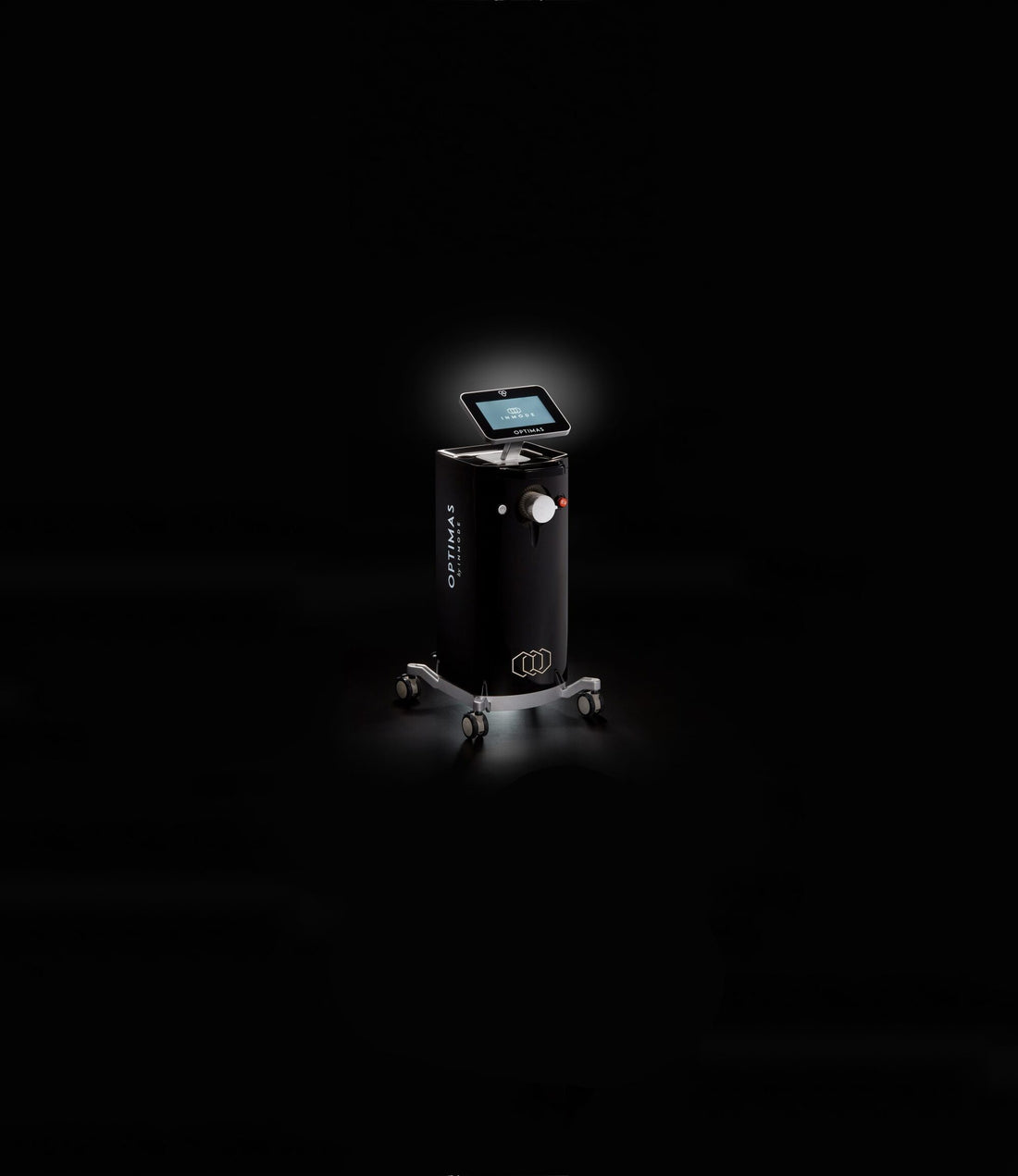 A sleek, modern floor-standing Optimas coffee machine on wheels illuminated by a spotlight against a dark background. The Optimas features a touch screen interface and is part of a full beauty suite, complete with a coffee cup dispenser.