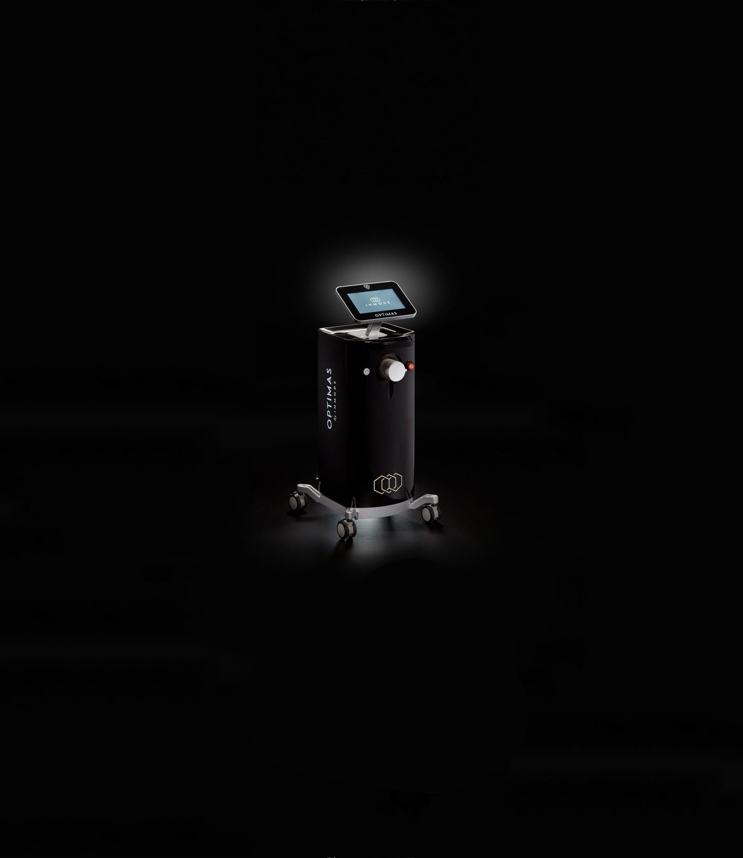 A sleek, modern floor-standing Optimas coffee machine on wheels illuminated by a spotlight against a dark background. The Optimas features a touch screen interface and is part of a full beauty suite, complete with a coffee cup dispenser.