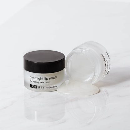 Image of an overnight lip mask by PCA Skin. The product, which comes in a small jar with a black lid, is labeled &quot;HA Lip Overnight Mask.&quot; The jar is shown both closed and open, with some of the clear gel-like mask oozing out onto a white marble surface.