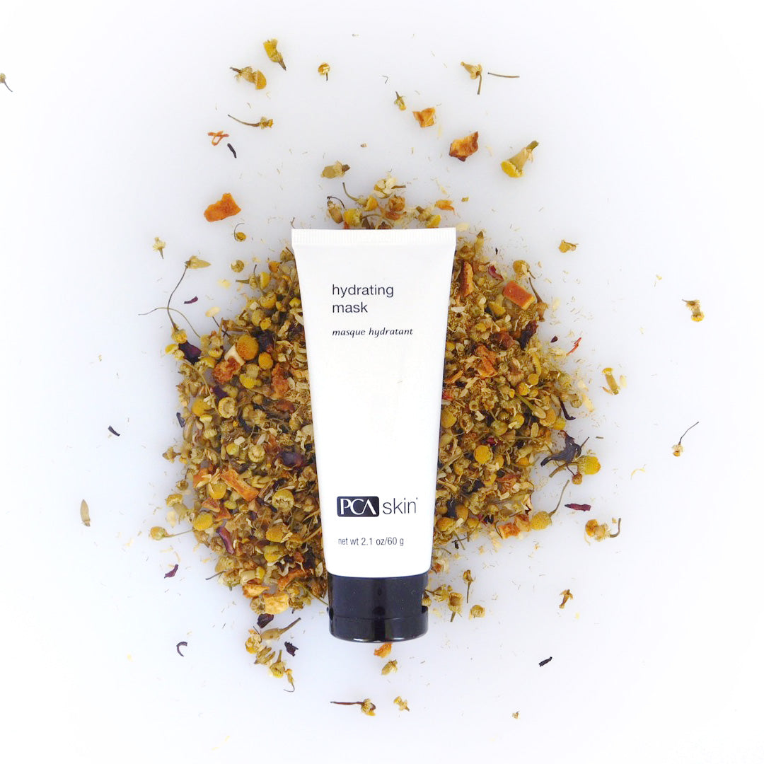 A white tube labeled &quot;Hydrating Mask&quot; from PCA Skin is placed upright on a bed of dried floral petals and herbs. The background is a clean, white surface, enhancing the natural and refreshing aesthetic of this skincare product designed for optimal skin moisture retention.