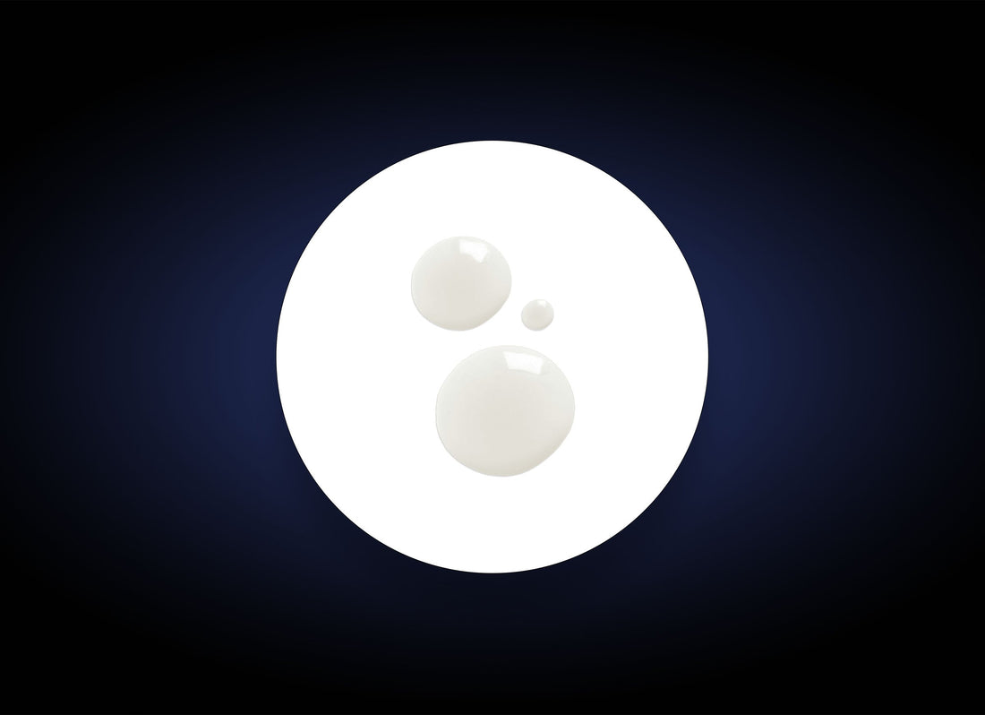 A white circle featuring three smaller white droplets of varying sizes on its surface, positioned against a dark gradient background. The droplets, resembling biodegradable exfoliants in Daily Exfoliant, are placed somewhat asymmetrically within the circle.