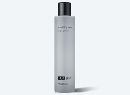 A transparent frosted bottle of Smoothing Toner, infused with aloe and lactic acids, featuring a sleek black cap. The label is simple, displaying the product&