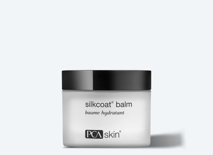 The image shows a jar of Silkcoat Balm, an advanced moisturizer designed for ageing skin. The white jar with a black lid features text that reads &quot;silkcoat® balm,&quot; &quot;baume hydratant,&quot; and bears the PCA Skin logo. The light gray background accentuates the jar&