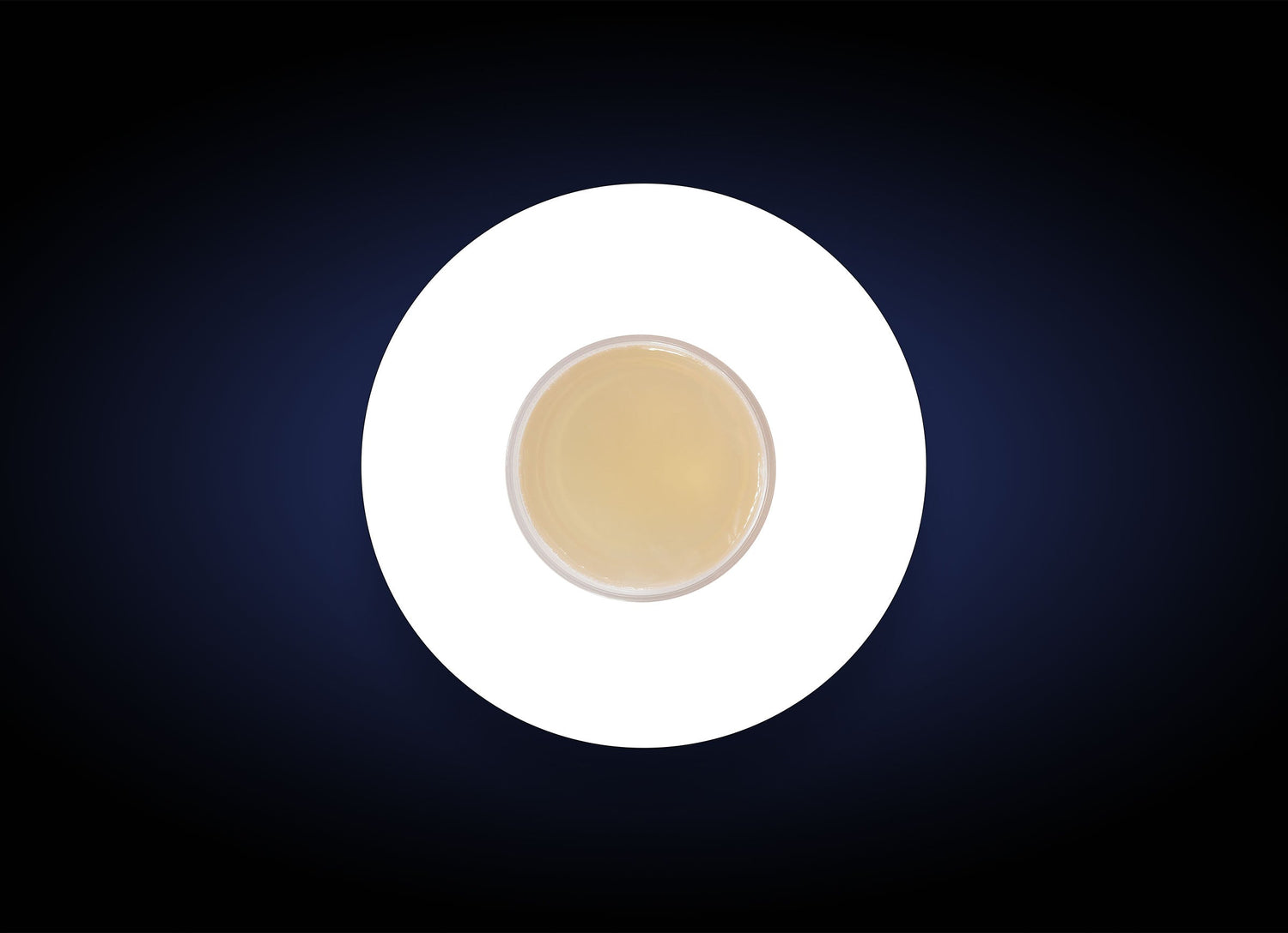 A top-down view of a cup filled with a light beige liquid, possibly tea or coffee, placed on a white circle against a dark background. The contrast between the white circle and dark backdrop highlights the cup centrally, akin to how the Blemish Control Bar targets acne breakouts on oily skin.