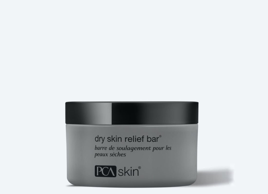 A gray cylindrical container with a black lid labeled "Dry Skin Relief Bar." The image features the text in both English and French against a light background, highlighting its effectiveness as a gentle cleansing bar for dry skin.