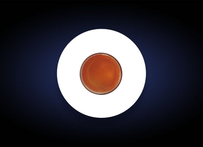 A top-down view of a round glass of tea or coffee, placed in the center of a white circular surface. The background surrounding the white circle is dark blue, creating a contrast with the white and the brown color of the beverage, reminiscent of how a Dry Skin Relief Bar contrasts with dry skin.