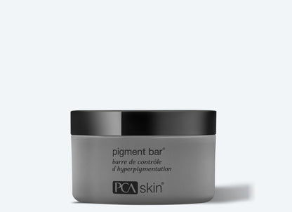 A gray jar of Pigment Bar with a black lid, designed for hyperpigmentation control and even skin tone. The text on the jar reads &quot;pigment bar&quot; and &quot;barre de contrôle d’hyperpigmentation&quot; above the &quot;PCA skin&quot; logo at the bottom. The background is light gray.