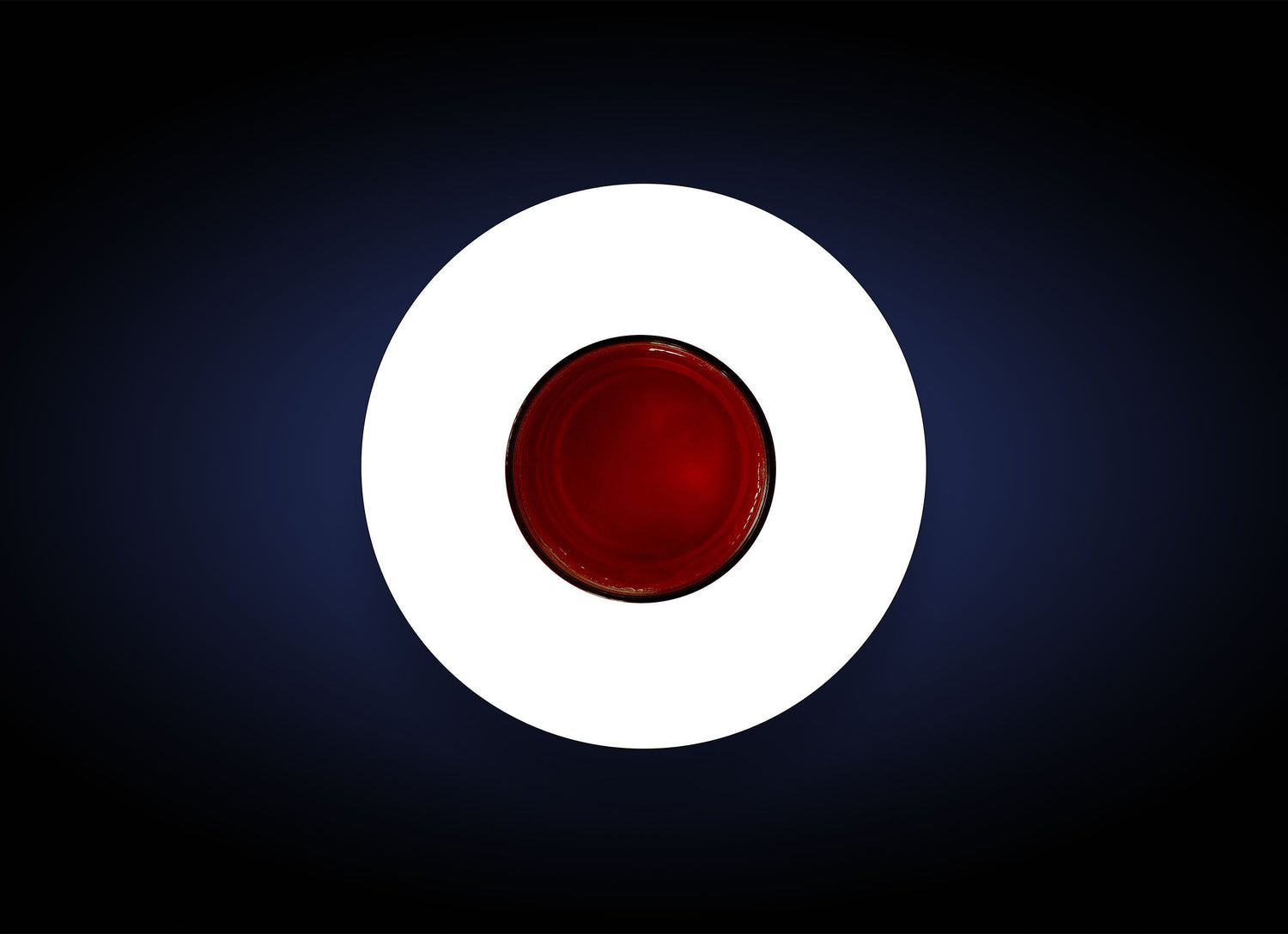 Aerial view of a round, red object centered on a dark blue background with a white circular border around it. The red object, resembling a glossy Pigment Bar, creates a striking visual effect with its vibrant color contrast and polished finish.