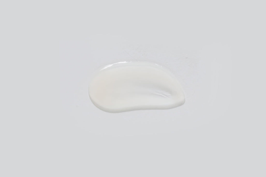 A small, irregular puddle of clear, milky-white Rejuvenating Serum 30ml rests on a plain light gray background.