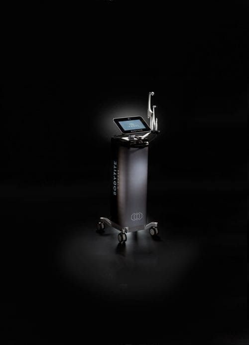 A Bodytite medical device with a touch screen on a tall, wheeled stand displays an interface with buttons and data. Various instruments and attachments for radiofrequency body contouring are affixed to the machine. The black background highlights the device.