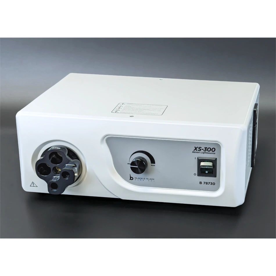 A white Onyx-Lite XS-300, 300 Watt Xenon Light Source features various controls and dials, including a power switch and a large, circular component on the left side. With 300 Watt Xenon Light for superior illumination in the surgical field, it rests on a dark surface against a dark background.