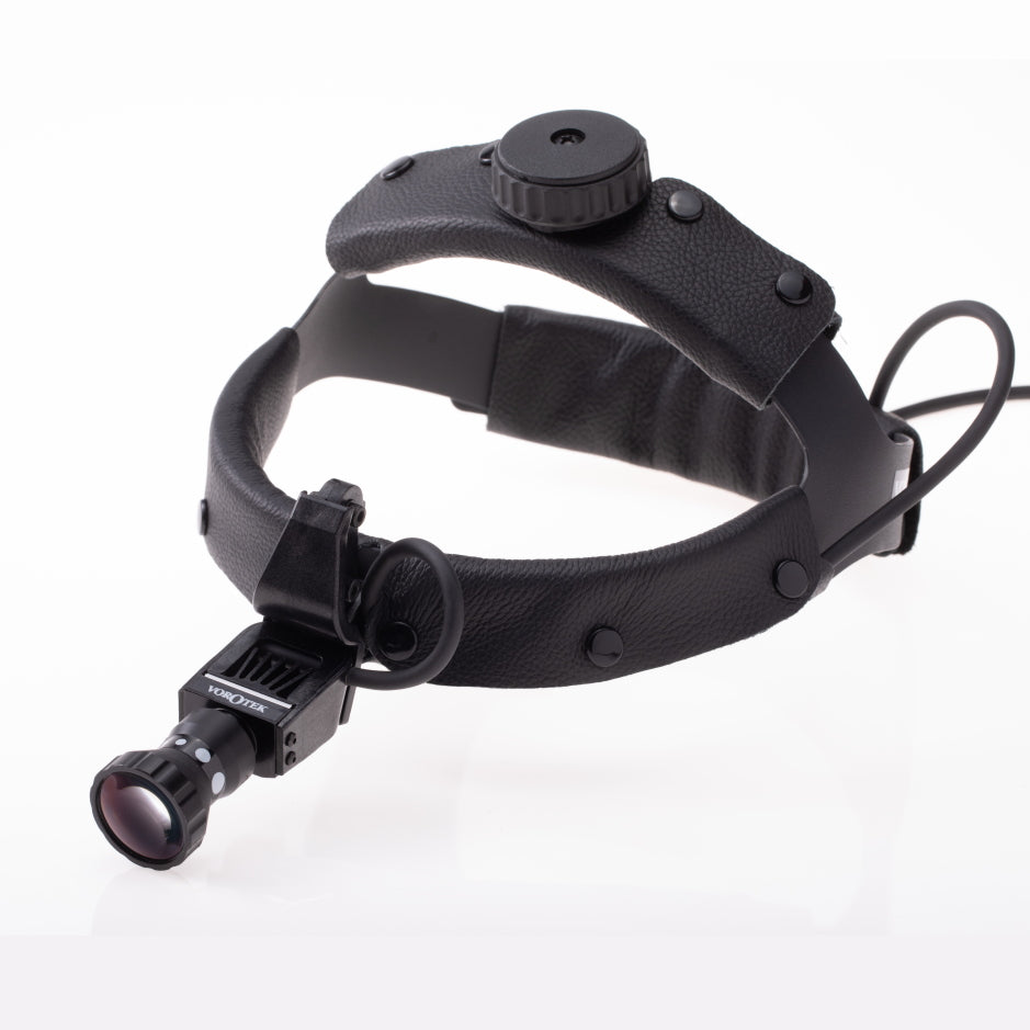 A black, adjustable headband with an attached monocular device is shown. The headband features padding, multiple buttons or knobs for adjustments, a connected wire, and an Adjustable Spot Vorotek LED Headlight. The monocular attachment is positioned at the front for magnification or enhanced vision.