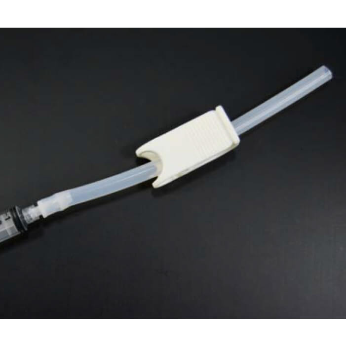 A Silicone Transfer Tube With C-Clamp And Luer Fitting connected to a syringe is secured with a white plastic clip against a dark background.