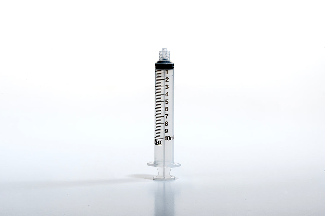 A 10cc Luer BD Syringe marked with measurements from 1ml to 10ml stands vertically against a white background. The Luer tip syringe is devoid of a needle and is capped at the top, displaying graduated markings for precise liquid measurement.