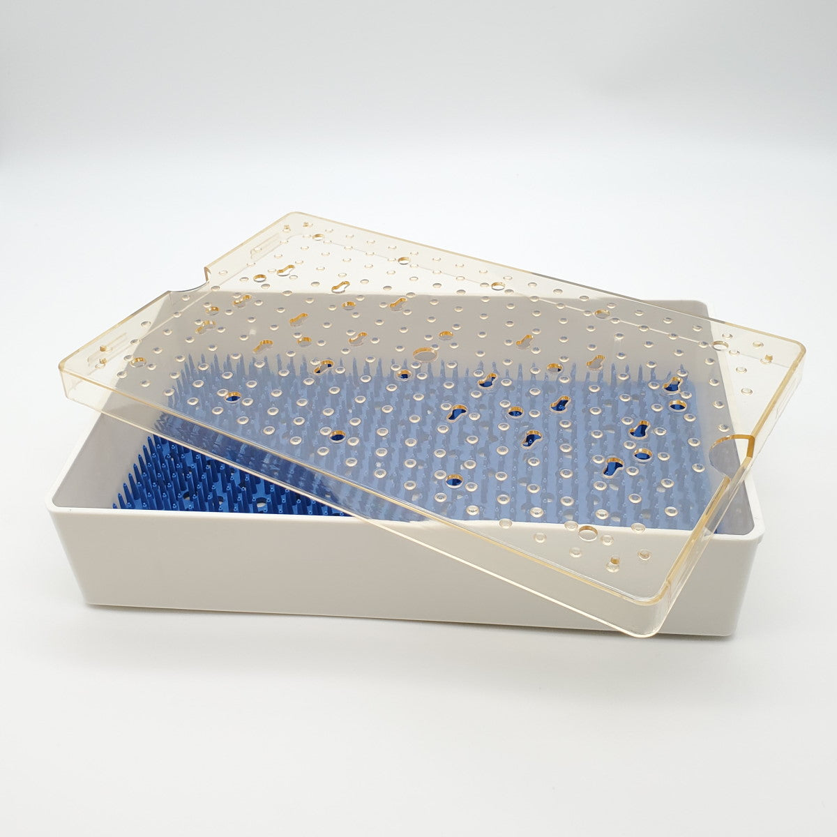 A white rectangular Sterilization Tray Single Level; Base, Lid, Mat with a blue spiked base for holding dishes upright, designed similarly to an instrument tray. It features a transparent lid with water droplets on it, propped up against the side of the rack. The background is plain white.