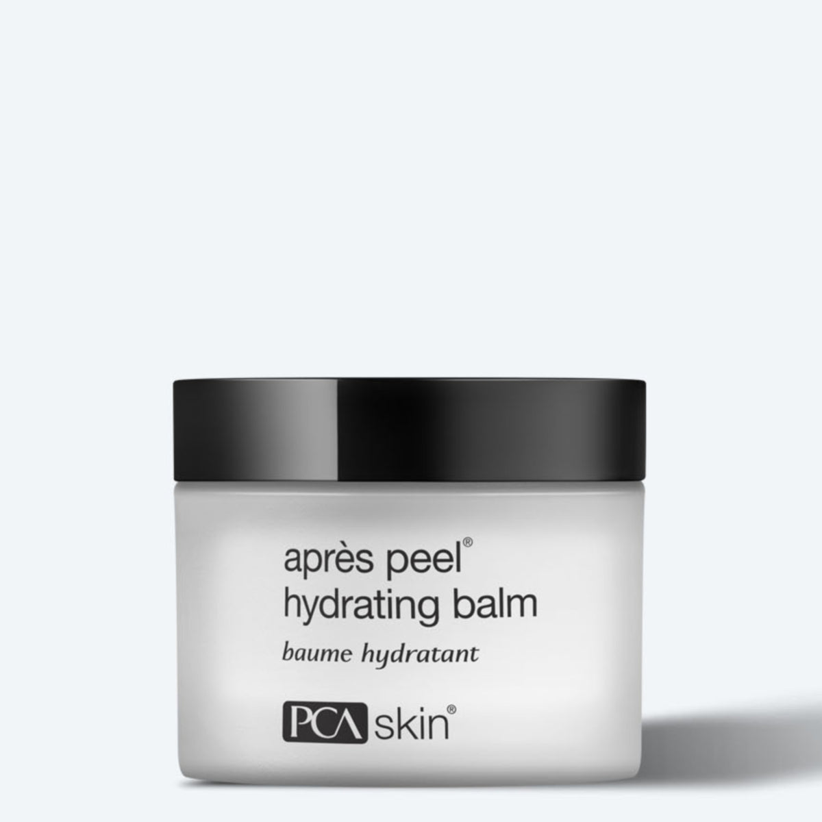 A white cosmetic jar with a black lid, labeled &quot;Aprés Peel Hydrating Balm&quot; and &quot;Baume Hydratant&quot; by PCA Skin. The container, designed for aging skin and fine lines, features a minimalist design against a light gray background.