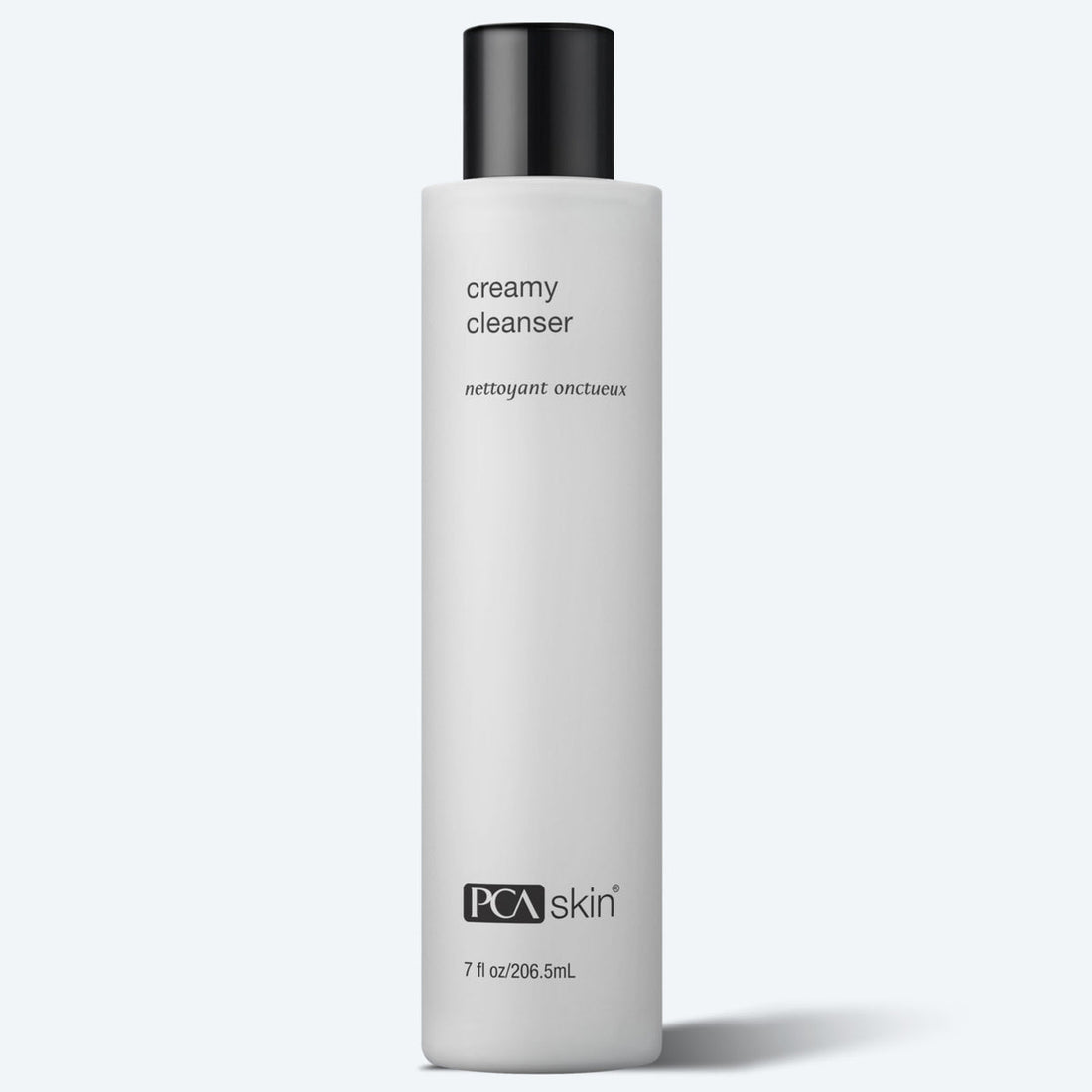 A white cylindrical bottle with a black cap labeled "Creamy Cleanser" in both English and French text. The bottle features the brand name "PCA skin" at the bottom and indicates the volume as "7 fl oz/206.5ml." Perfect for dry and sensitive skin, this moisturizing cleanser is set against a light grey background.